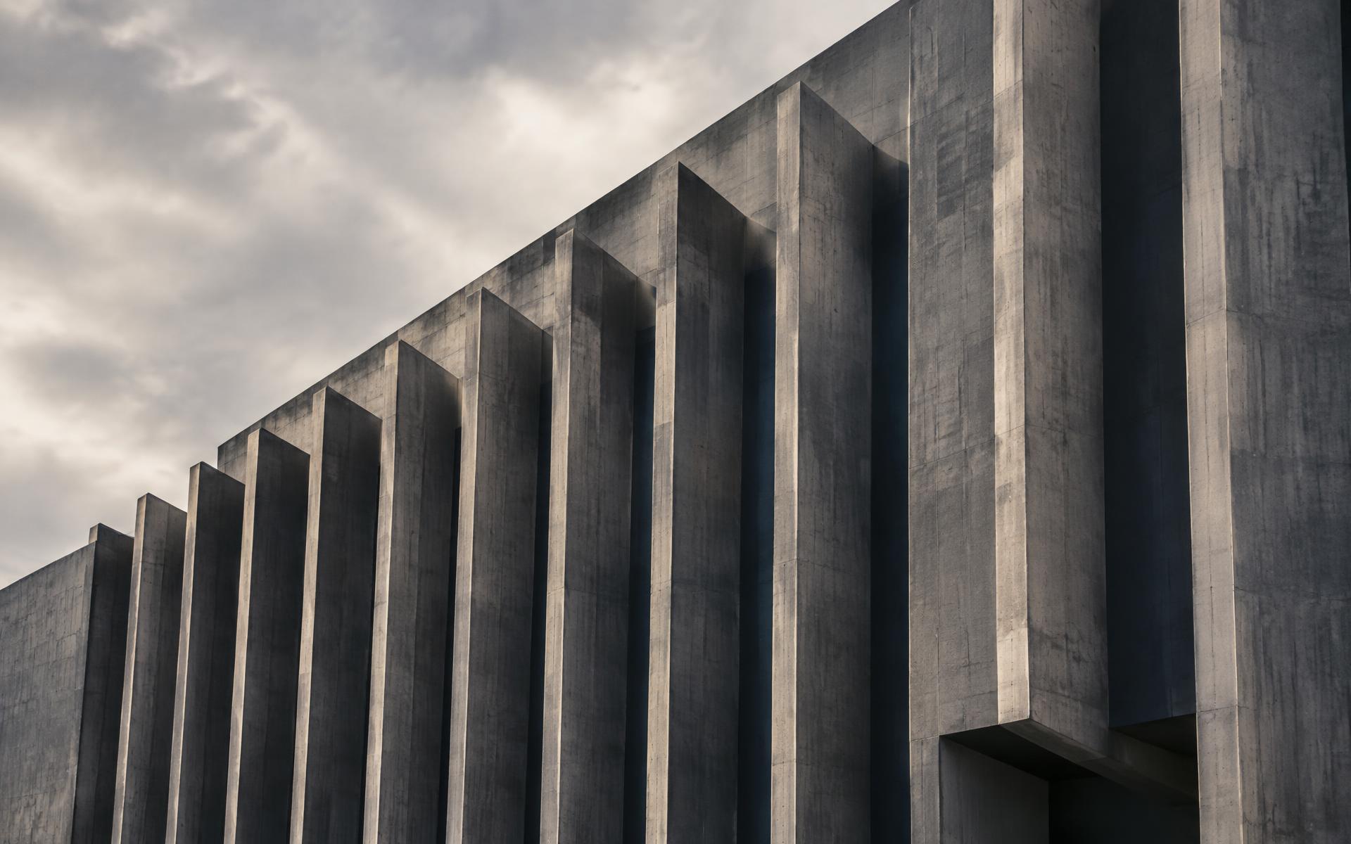 Concrete facade of repeated vertical fins receding into overcast sky